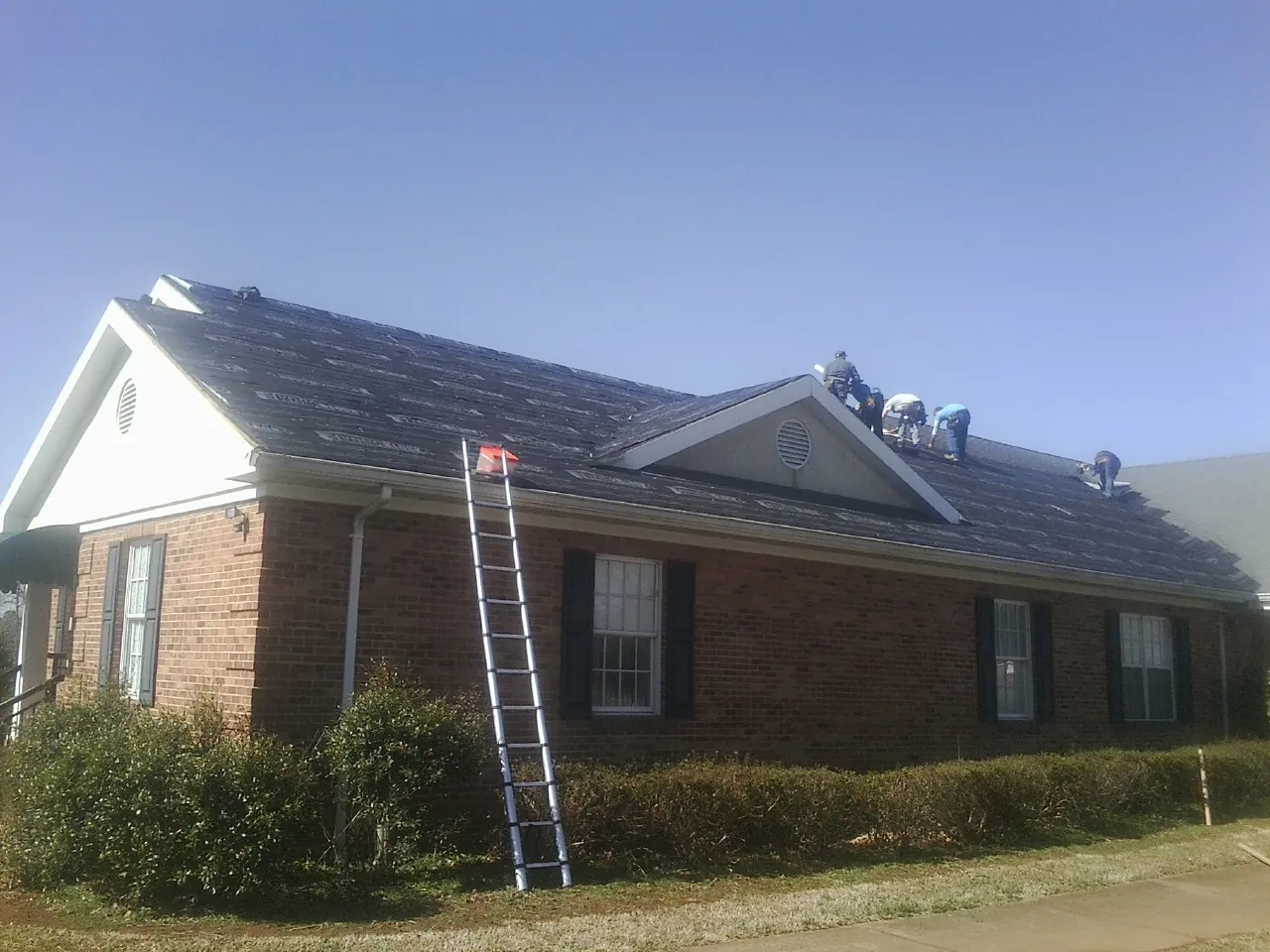 Crew tearing shingles off a brick ranch roof with a ladder set — Emergency Roof Repair work by our crew in Agness
