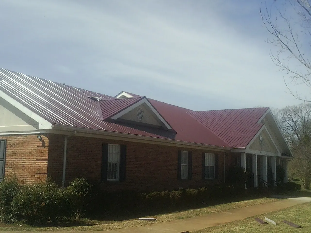 Red metal roof with gabled entries on a long brick building, from a Hail Damage Roof Repair job in Agness