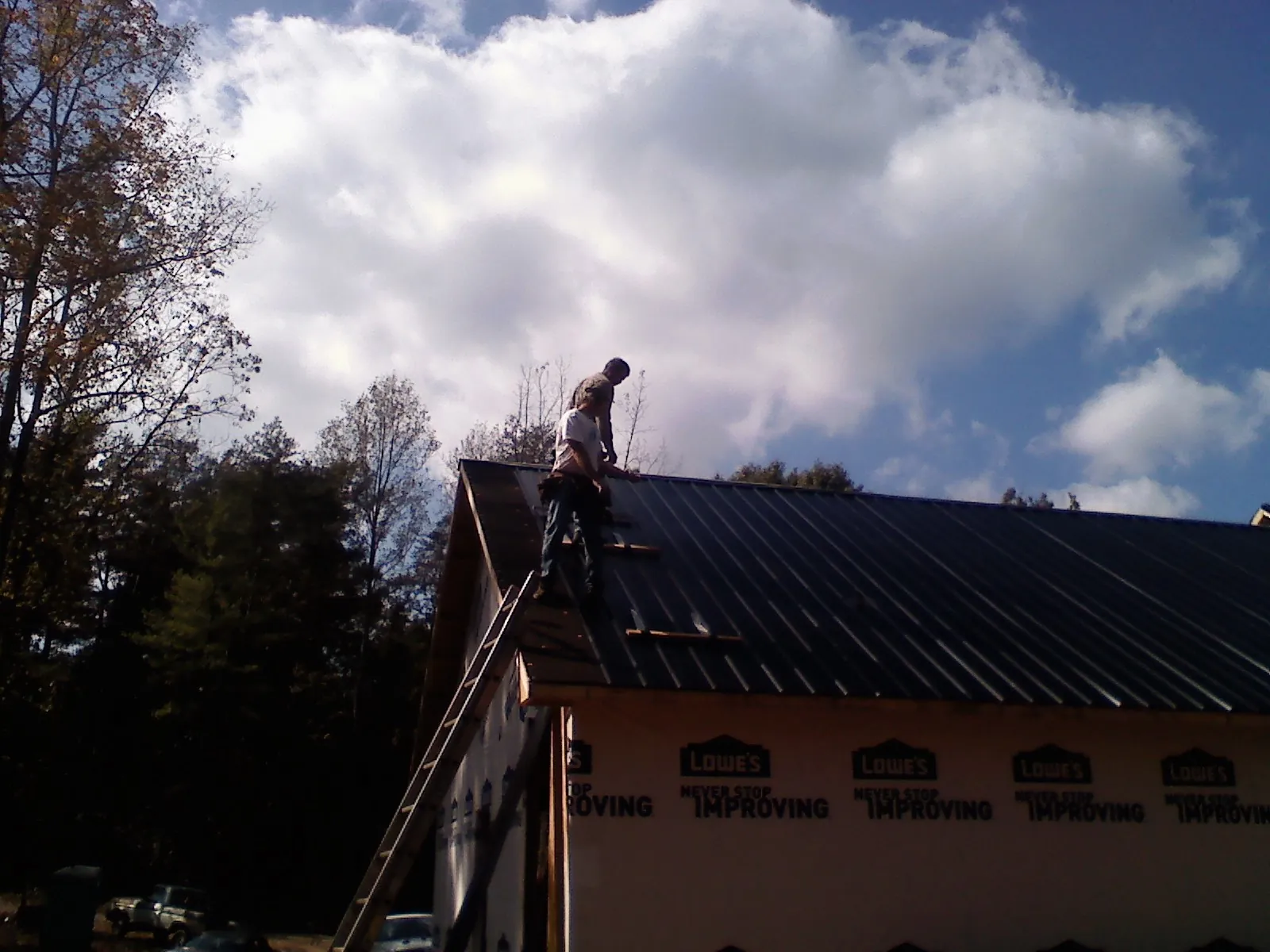 Roofer fastening dark metal panels high against a cloudy sky, from a Roof Inspection job in Agness