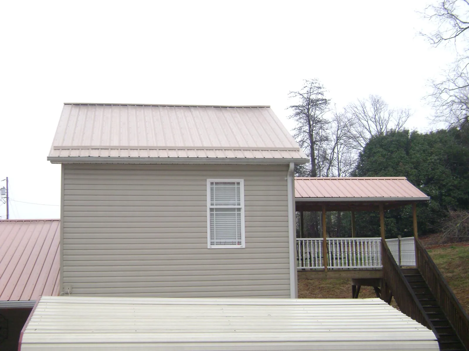 Tan metal roofs on a two story addition and attached porch, from a Roof Replacement job in Agness